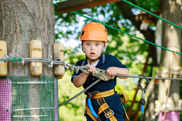 Un niño con síndrome de Down realiza deportes en una carrera de obstáculos, un niño en un casco en un parque infantil, niños en desarrollo previo. - Foto, imagen