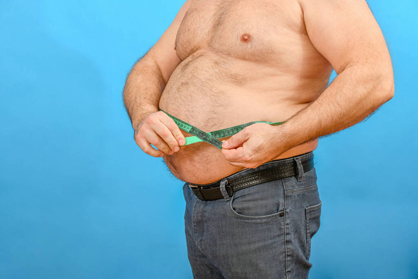 Ein Mann in Jeans misst eine große, dicke Taille mit einem grünen Zentimeter. - Foto, Bild