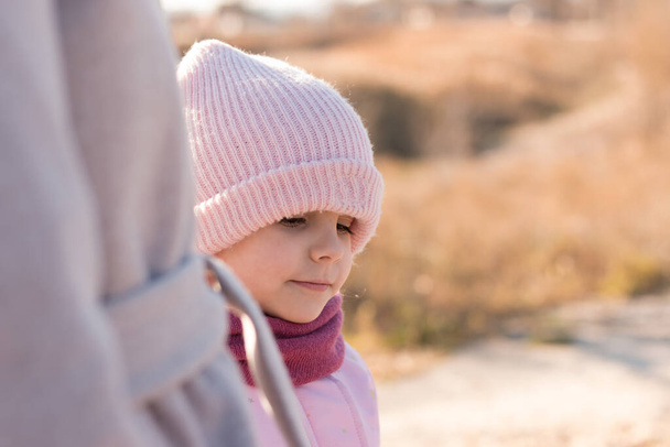 A small child in a funny hat and scarf holds a parent's hand on a walk outdoors - Foto, immagini