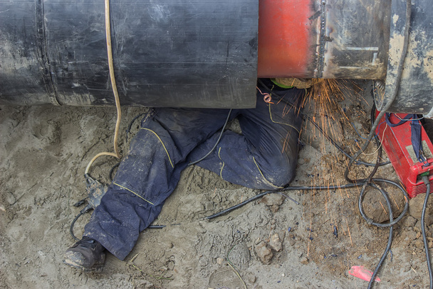 Welder worker grinding the weld in trench under pipeline - Photo, Image