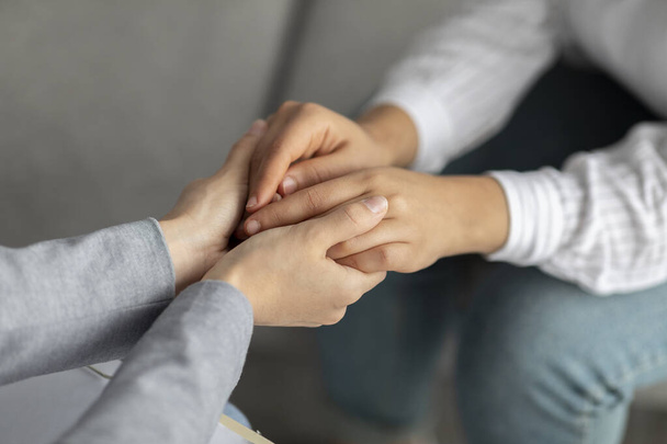 Психологічна підтримка. Психотерапевт пропонує допомогу молодій жінці, тримаючись за руки під час сеансу психотерапії
 - Фото, зображення