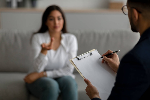 Mujer árabe estresada consultando psicóloga en consultorio médico, psiquiatra tomando notas durante la sesión - Foto, imagen