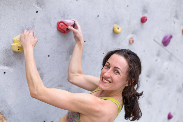Menina sorridente sobe a parede de escalada, a mulher está envolvida em esportes radicais, escalada na cidade, força e treinamento de resistência - Foto, Imagem
