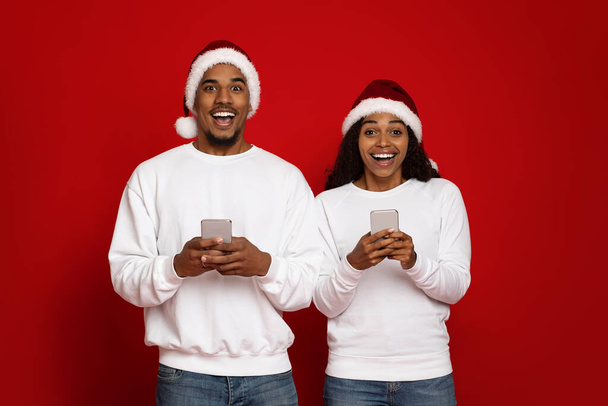 Beautiful black couple in Santa hats using smartphones - 写真・画像