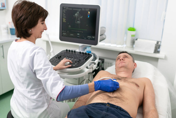 Doctor usando una máquina de ultrasonido para escanear el corazón de un paciente masculino. El cardiólogo hace de un paciente una prueba ecocardiográfica en una clínica. Paciente sometido a ecografía en el hospital - Foto, Imagen