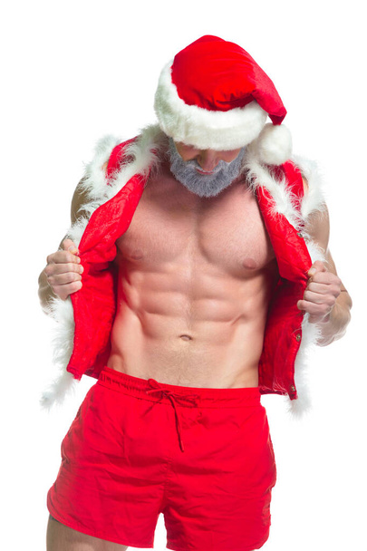 Christmas. Portrait of muscular sexy strong athlete in Santa Claus costume with gray beard posing showing his abs isolated on white background - Fotó, kép