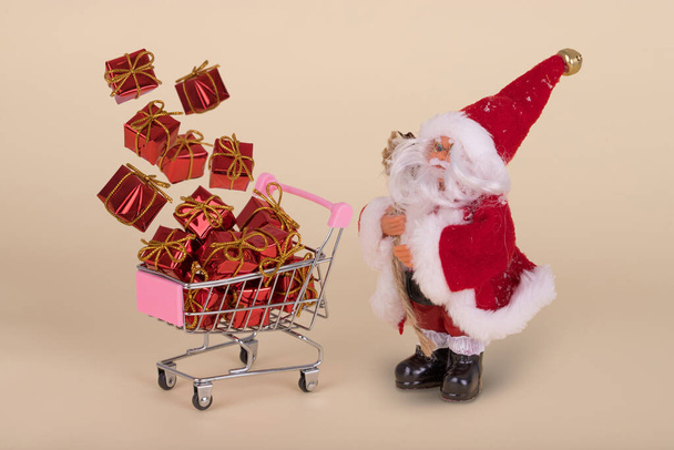 Santa Clause and Shopping cart or trolley with flying gifts on a beige background. Minimal Christmas sale composition. Happy holidays. New year minimal concept - Photo, Image