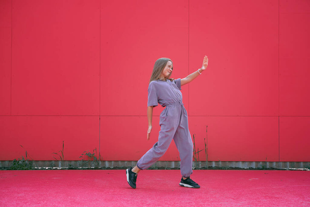 Active teen girl dancing outdoors on red wall background. Stylish modern young dancer perform contemporary hip hop dance - 写真・画像