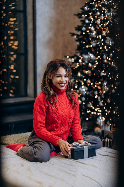 Kobieta uśmiecha się jasno trzymając prezent świąteczny i pozowanie - Zdjęcie, obraz