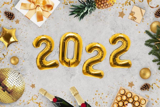 Πολυτελής Πρωτοχρονιά 2022 κόμμα. Χρυσή μπαλόνια 2022 βρίσκεται σε γκρι φόντο με χρυσό καθρέφτη μπάλα, καραμέλα, σαμπάνια, δώρα, ανανάς, χριστουγεννιάτικο δέντρο και καραμέλα, κορυφαία άποψη. Γιορτές. - Φωτογραφία, εικόνα