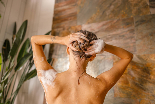 Вид ззаду гола молода жінка миє волосся, приймаючи душ у ванній
 - Фото, зображення