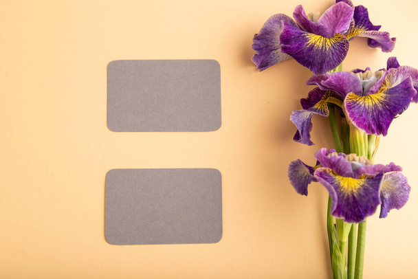 Γκρι επαγγελματική κάρτα με πασχαλιά ίριδας λουλούδια σε πορτοκαλί παστέλ φόντο. Κάτοψη, οριζόντια θέση, αντίγραφο χώρου, νεκρή φύση. Πρωινό, πρωί, ανοιξιάτικο. - Φωτογραφία, εικόνα