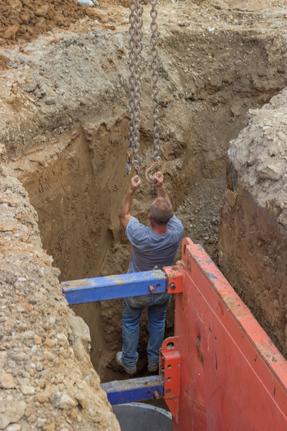 Excavator arm lifting construction worker from trench on chains - Photo, Image