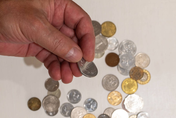 Bent coin in hand of a man on blurred background of coins on white table - Photo, Image