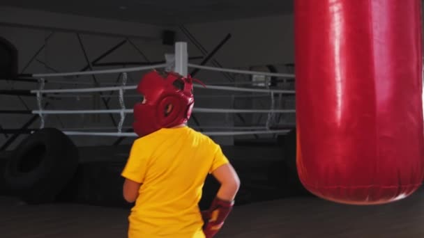 Kleine jongen in beschermende helm schoppen de bokszak uit de bocht - Video
