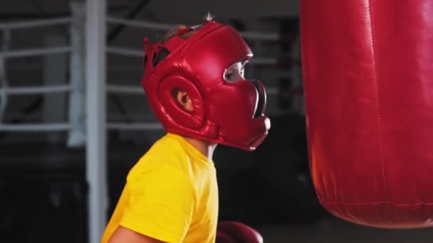 Маленький мальчик в защитном шлеме ударяется о боксерскую грушу - Кадры, видео