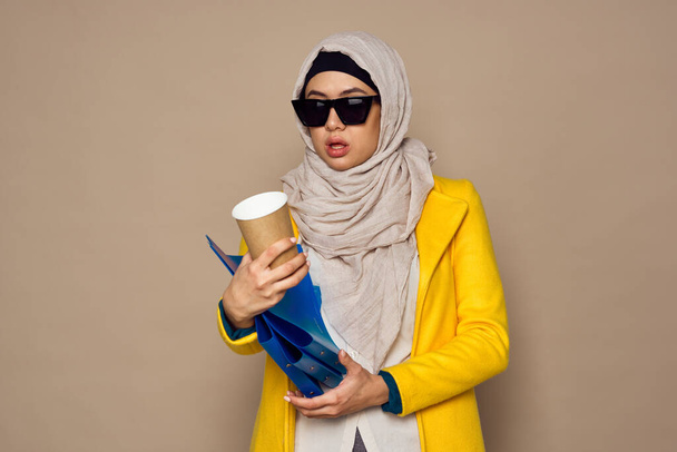 woman in sunglasses in hijab a cup of coffee beige background - Foto, Imagem