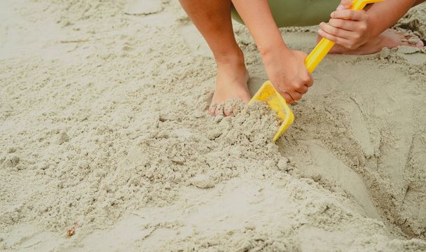Gyerek játszik homok sárga lapát a strandon. - Fotó, kép