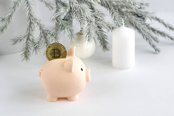 Metallic gold-colored bitcoin coin in a piggy bank pink pig on the background of a Christmas tree, candles, a place to place text. Finance, investments, virtual money - Valokuva, kuva