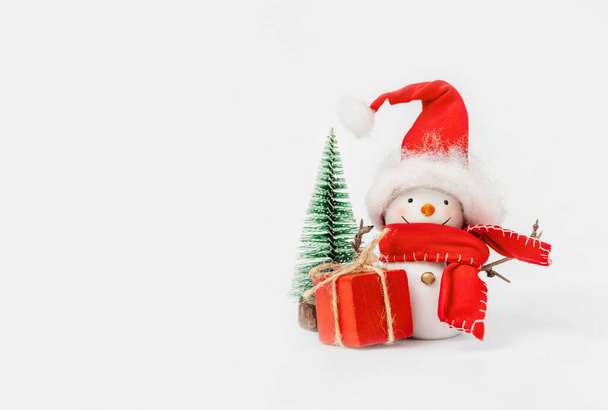 Muñeco de nieve feliz con un regalo cerca del árbol de Navidad en el fondo blanco - Foto, Imagen