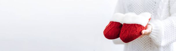 Mujer en suéter blanco sostiene cálidas zapatillas de punto rojo. Concepto de hogar familia vacaciones acogedoras Navidad Año Nuevo. - Foto, imagen