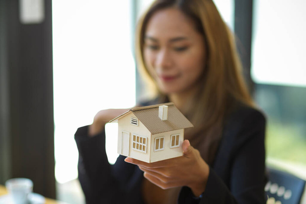 Image en gros plan d'une agente immobilière tenant un modèle de maison au bureau. Concept d'homme d'affaires - Photo, image