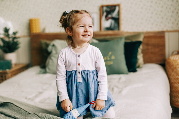A smiling girl is sitting on a bed in a room decorated for Christmas and New year, the baby is enjoying the holidays - Φωτογραφία, εικόνα