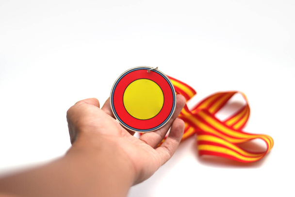 Graduation medal with an empty circle-shaped medal and red-yellow stripes ribbon on hand isolated on white background. Education, sport, champion, winners concept background stock images. - Photo, Image