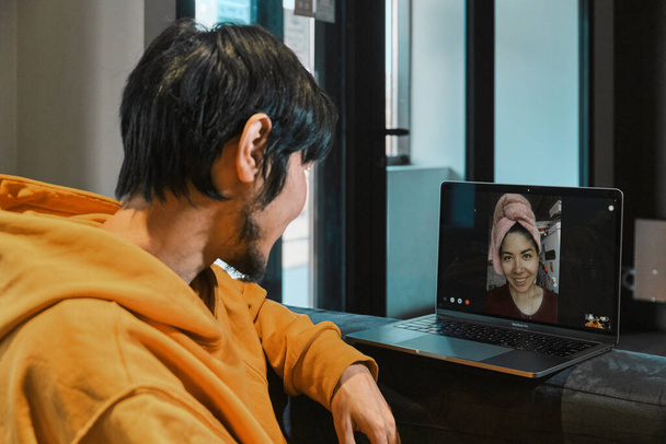 Asyalı bir adam küçük bir ofiste oturuyor ve kız arkadaşıyla laptopla iletişim kuruyor. - Fotoğraf, Görsel