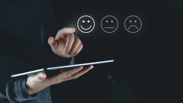 Close-up van de mens klant aanraken van het virtuele scherm op de vrolijke glimlach gezicht pictogram om tevredenheid te geven Beoordeling, Service rating, tevredenheid, Customer service experience, en tevredenheid enquête concept - Foto, afbeelding
