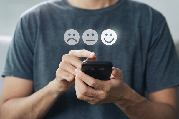 Close up of man customer touch smartphone screen on the happy Smile face icon to give satisfaction. Recenze, hodnocení služeb, spokojenost, zkušenosti se zákaznickým servisem a koncepce průzkumu spokojenosti. - Fotografie, Obrázek