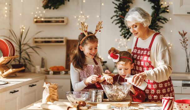 Two little kids making Christmas homemade cookies together with elderly grandmother in kitchen - Valokuva, kuva