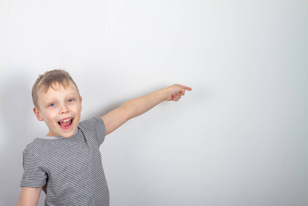 Cheerful caucasian boy smiles and points with his finger on a gray background - Foto, imagen