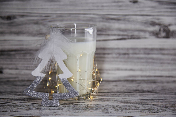 Leuke kersttraditie. Handgemaakte verse koekjes en warm glas melk op de houten tafel. Tafelopstelling. Feestelijke kerststemming en esthetische sfeer met bloemenslingers. Kopieerruimte - Foto, afbeelding