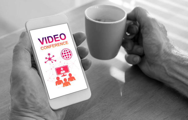 Mannelijke handen met een smartphone met videoconferentie concept en een kopje koffie - Foto, afbeelding