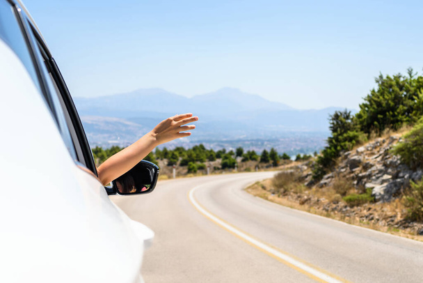 Woman sticking hand out from the open window driving a car. Trip on the serpentine road in the mountains. Summer vacation. Freedom concept. copy space - Fotografie, Obrázek