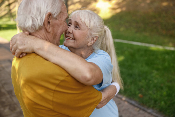 Hymyilevä kypsä nainen miehensä kanssa urheiluvaatteet halata vihreässä puistossa - Valokuva, kuva