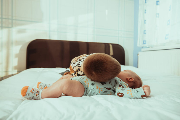 An adorable toddler lying on a bed with his cute newborn sibling - Photo, Image