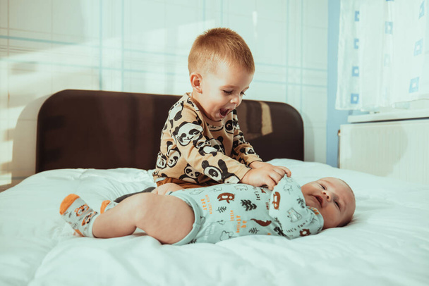 An adorable toddler playing with his cute newborn sibling on a b - Fotó, kép