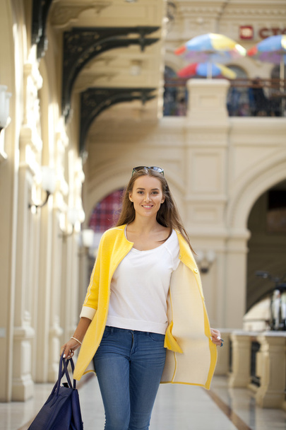Young woman in yellow coat walking in the shop - 写真・画像