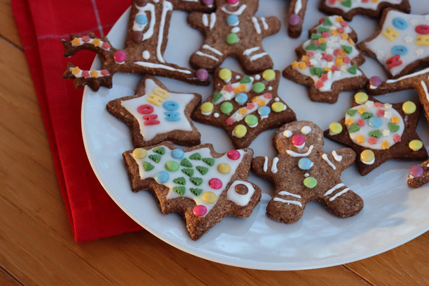 Homemade Christmas glazed and decorated cookies in various shapes on plate on wooden table  - Φωτογραφία, εικόνα