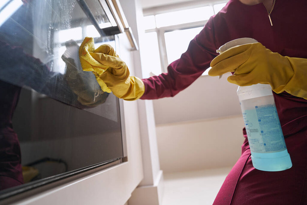 Professional housecleaner in rubber gloves cleaning part of electric cooker - Photo, Image