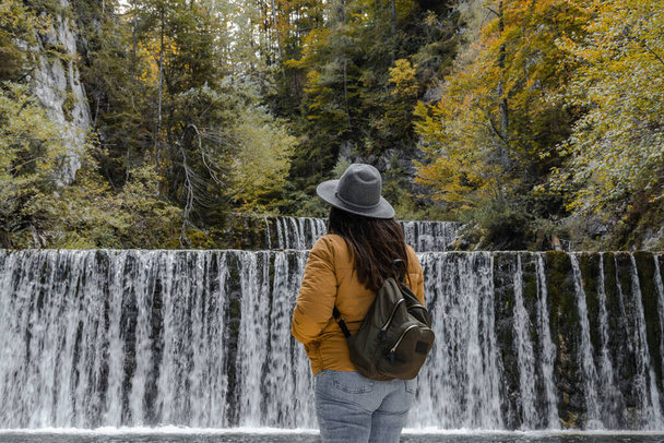 A Caucasian woman with autumn clothes and backpack standing in front of the waterfall - Foto, Bild