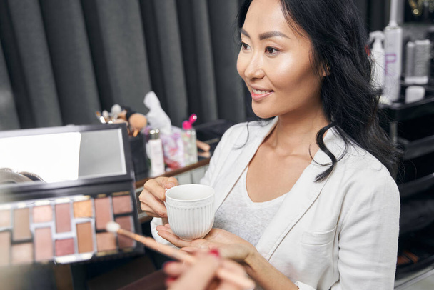 Elegante mujer asiática consiguiendo maquillaje profesional con cosméticos de lujo en el salón - Foto, imagen