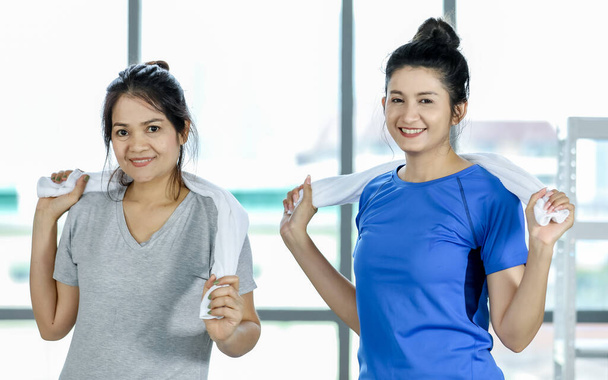 Urocze i zdrowe azjatyckie kobiety cieszyć wycieranie ramienia i szyi z uśmiechem i szczęśliwy, aby oczyścić pot przez ręcznik po zakończeniu treningu siłowego ciała i aktywności sportowej na siłowni w pomieszczeniach. - Zdjęcie, obraz