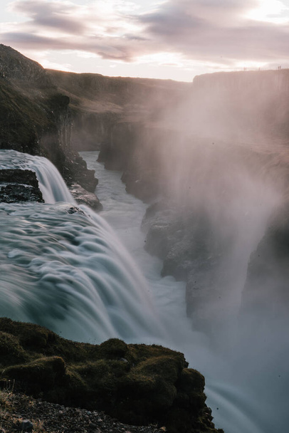 A vertical shot of the Gullfoss Falls with long exposure under a cloudy sky and sunlight in Iceland - Foto, Imagen