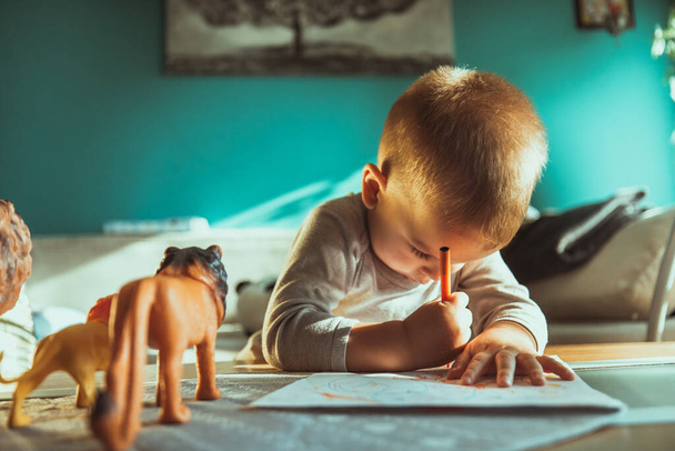 A shallow focus of an adorable toddler drawing with colorful pencils and paper on the table - Fotó, kép