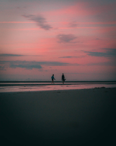 A vertical shot of the silhouettes of people at the beach during a beautiful sunset in the evening - Photo, Image