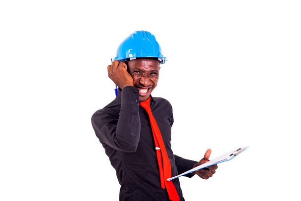 young man engineer wearing blue safety helmet and holding clipboard while smiling. - Фото, зображення