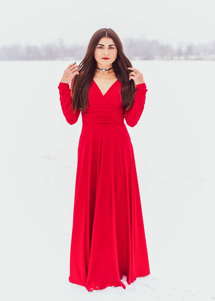 Mujer hispana bailando en vestido de seda en el día nevado, vestido rojo artístico ondeando y agitando tela, concepto de pasión - Foto, imagen